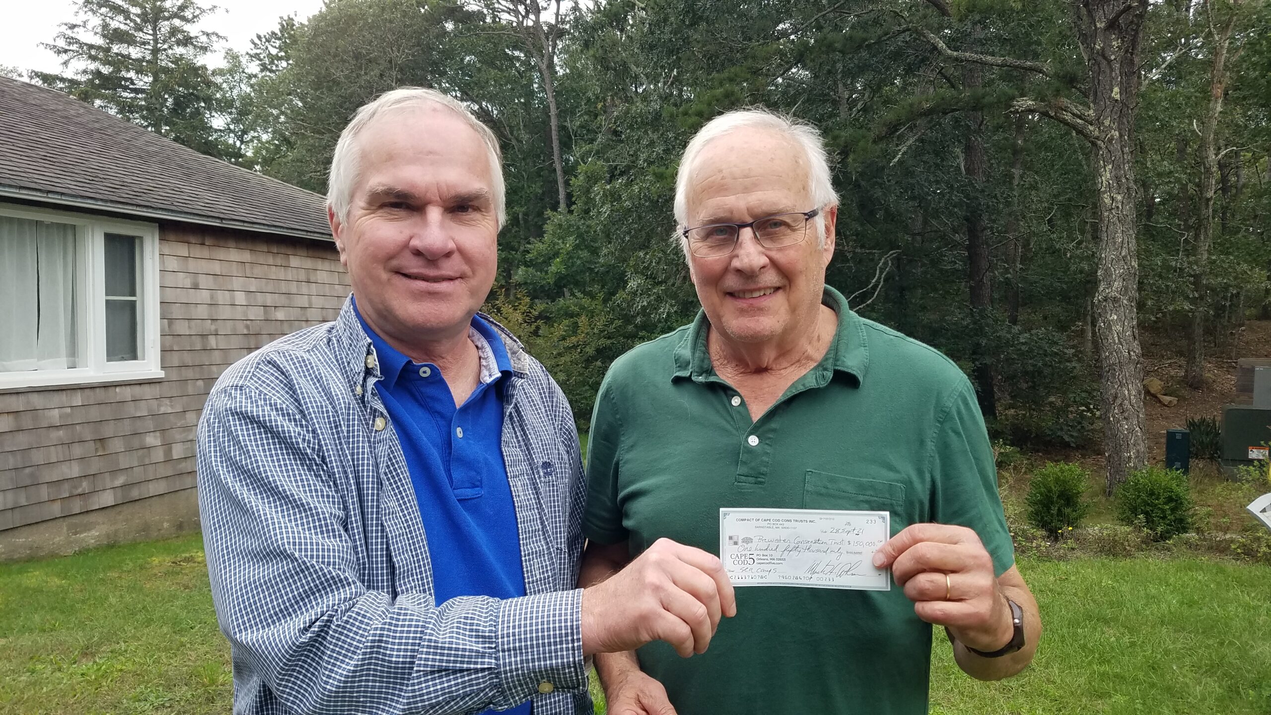 Two men holding a check outdoors